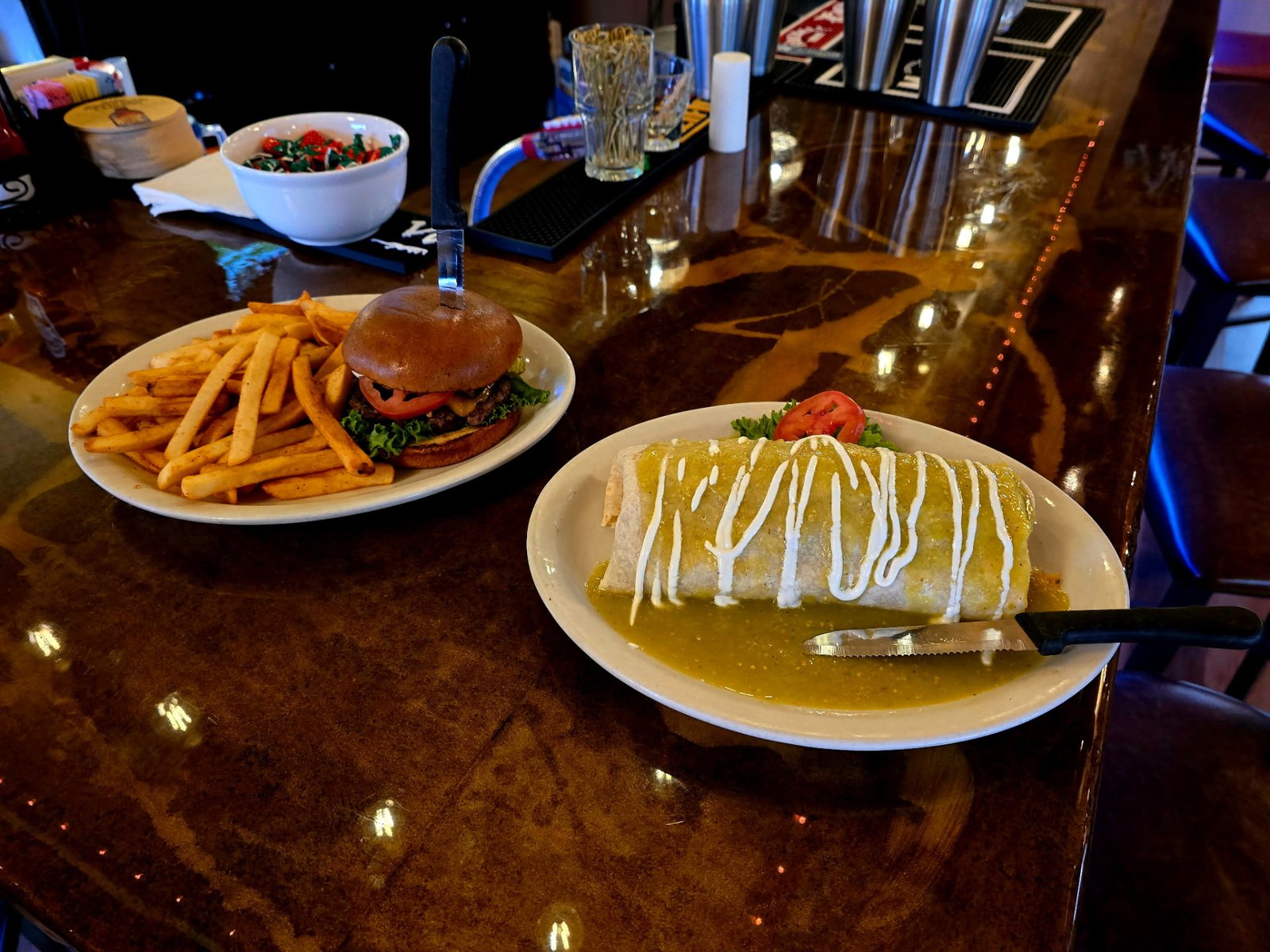 A cheeseburger with a pile of fries next to a smothered green chile burrito topped with sour cream
