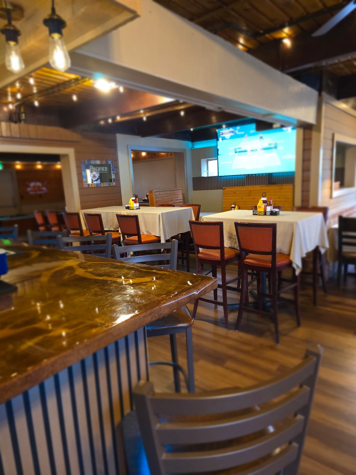 Dining room at Vista Lounge with linen-topped tables, rust leather chairs and a big screen showing the game